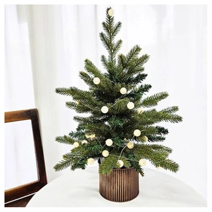 Detail of green artificial Christmas tree with warm LED globe lights in bronze pot