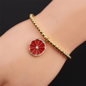 Detail of gold beaded bracelet with citrus pendant on female wrist in soft lighting