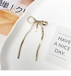 Close-up of golden bow-shaped hair clip with snake chain texture and long ribbon design