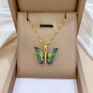 Detail of a golden butterfly pendant with blue-green gradient wings in a beige gift box
