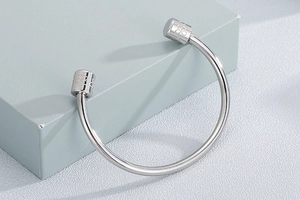 Close-up of silver steel open cuff bracelet featuring engraved clover on cylinder ends