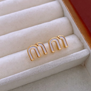 Macro shot of gold-plated earrings with letter M design and white enamel inlay
