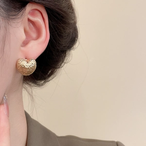 Close-up of golden heart earrings with hammered texture worn by a female model