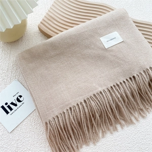 Detail of light camel knit scarf featuring a minimalist woven label and long soft tassels