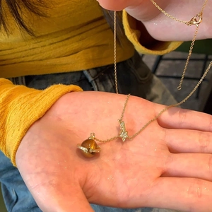 Golden necklace with zircon star and amber planet pendant held in hand for daily wear