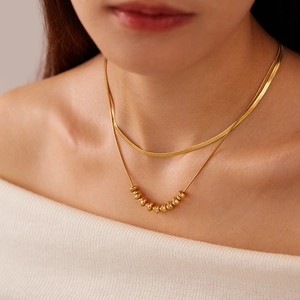 Close-up of double-layered gold snake chain necklace with bead charm on a model