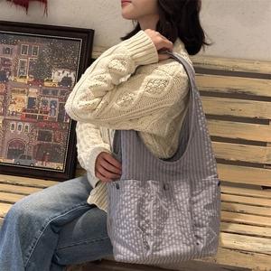 Close-up of a large grey gingham tote bag with outer pockets and metal button detail