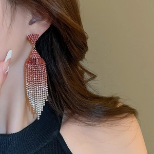 Close-up of long tassel earrings with pink gradient rhinestones in a geometric drop style