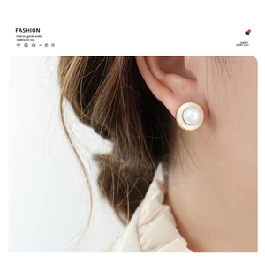Detail shot of a minimalist gold-rimmed pearl earring worn by a model in soft light