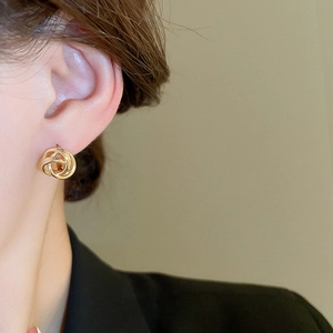 Close-up of a minimalist golden twisted metal earring worn by a model in a work suit