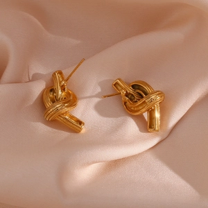 Detailed view of golden twisted knot stud earrings on luxurious champagne silk fabric