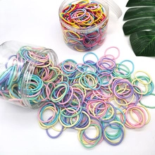 Colorful rubber hair ties for kids scattered from a container on a white surface