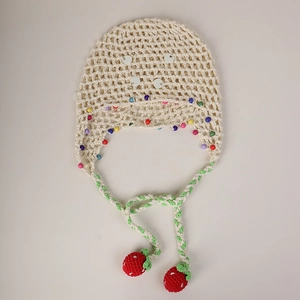 Detail of knit baby bonnet with colorful beads and handmade red crochet strawberry ties