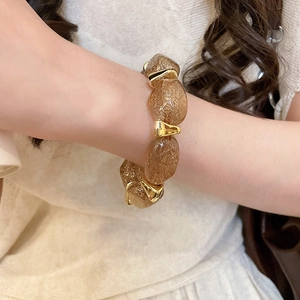 Detail showing amber resin beads with gold glitter and polished metal spacers on the wrist