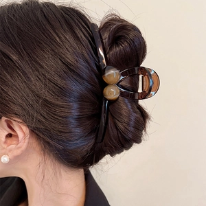 Close-up of a brown translucent acrylic hair claw with amber bead accents on model