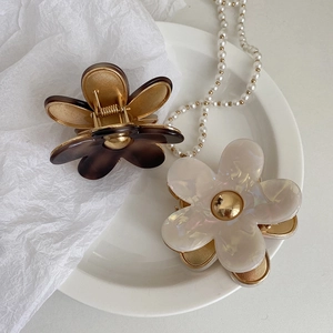 Detailed shot of acetate flower hair claws in tortoiseshell and pearl white with gold accents