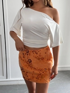 Detail of white one-shoulder draped top paired with an orange sequined floral mini skirt