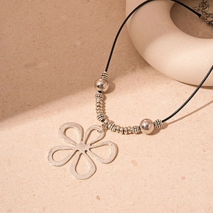 Macro detail of a silver hollow flower pendant on a black cord necklace with metallic beads