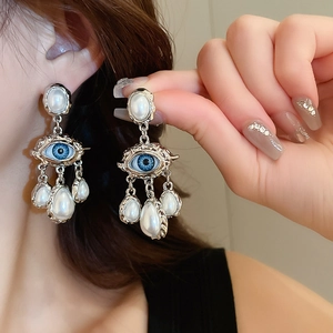 Detail of silver drop earrings featuring a blue evil eye motif and hanging teardrop pearls