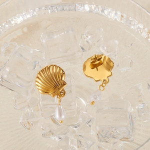 Detailed view of gold shell earrings with white pearl drops on crystal ice blocks