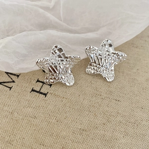 Macro detail of silver star stud earrings showing irregular textured metal surface