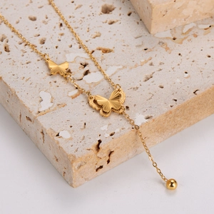 Collier pompon papillon doré en acier inoxydable posé sur une pierre de travertin beige