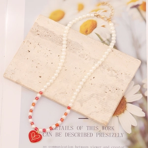 Handmade pearl necklace with red heart pendant on stone background, colorful beaded jewelry