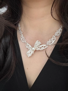 Vue détaillée du collier à nœud argenté avec perle sur un modèle en robe noire élégante