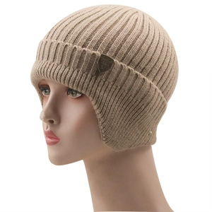 Detailed view of beige ribbed knit winter hat with ear flaps and metal shield badge