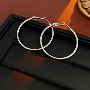 Close-up of silver hoop earrings with polished mirror finish on black leather texture