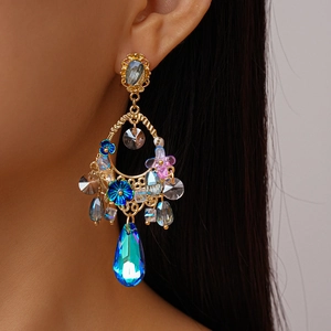 Close-up of golden floral earrings with blue teardrop crystals worn by a model