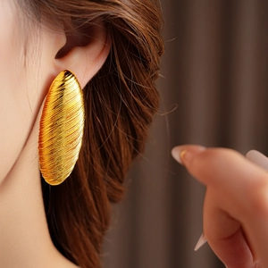 Detailed view of large gold oval earring with textured metal wire finish on model