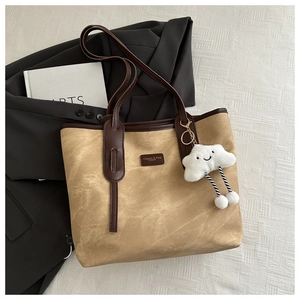 Detail of khaki canvas tote bag with brown trim and a white plush cloud charm accessory