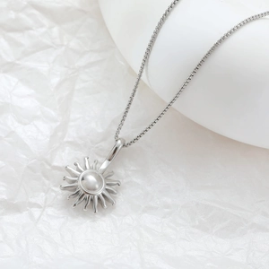 Minimalist silver sunburst pendant necklace in stainless steel on white textured background