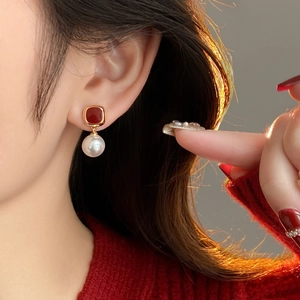 Detail of elegant red square stud earrings with white pearl drops on a model