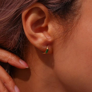 Gros plan détaillé d'une boucle d'oreille huggie dorée avec un zircon vert rectangulaire