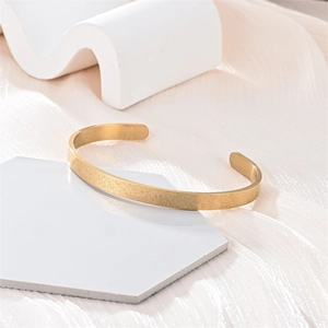 Detalle de brazalete abierto en forma de C dorado con una textura esmerilada elegante