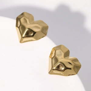 Macro shot of gold heart stud earring with geometric faceted texture on white background