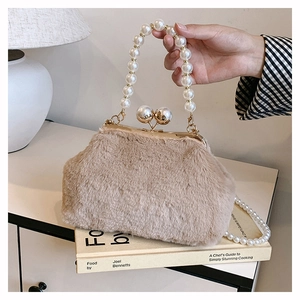 Plush beige handbag with pearl handle and metal clasp displayed on a book in home setting