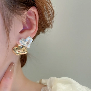 Close-up of asymmetric heart stud earrings in gold and silver finish on a model's ear