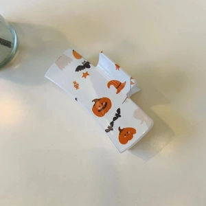 Detail view of square Halloween claw clip with pumpkin and bat prints on cream base