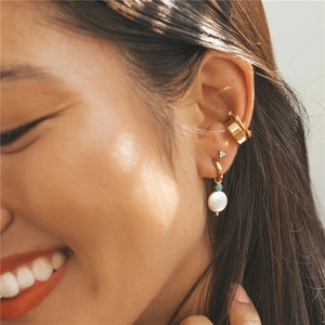 Close-up of gold ear cuffs and turquoise studs with pearl drop earrings on model