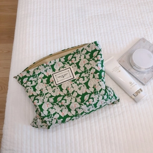 Floral green cotton makeup bag with white leaf patterns and a black square zipper tag