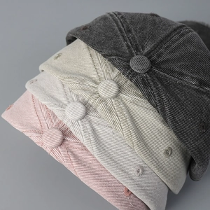Close-up of stacked cotton baseball caps in black, grey, beige and pink with fine stitching
