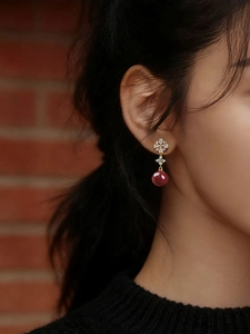 Close-up of model wearing red bead drop earrings with floral gold and zircon setting
