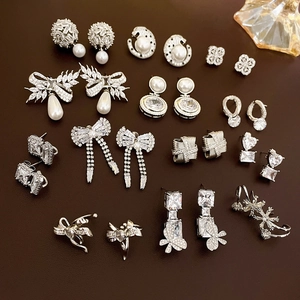 Detail of luxury zircon bow and flower earrings with pearls on dark leather background