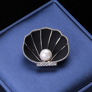 Macro shot of shell brooch with black enamel, a central pearl, and rhinestone accents