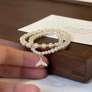 Close-up of double-layer pearl bracelet with a sparkling rhinestone fish tail pendant