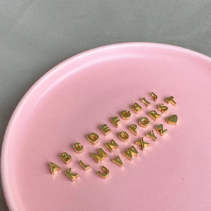 Macro view of gold S925 silver alphabet letters and heart pendant on a pink plate