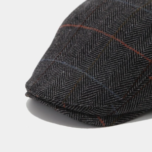 Detailed macro view of dark grey herringbone tweed flat cap with colorful weave patterns